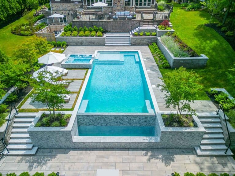 Illuminated home with well-lit steps, stone wall and uplights on trees in Short Hills, NJ, by Harmony Design Group.